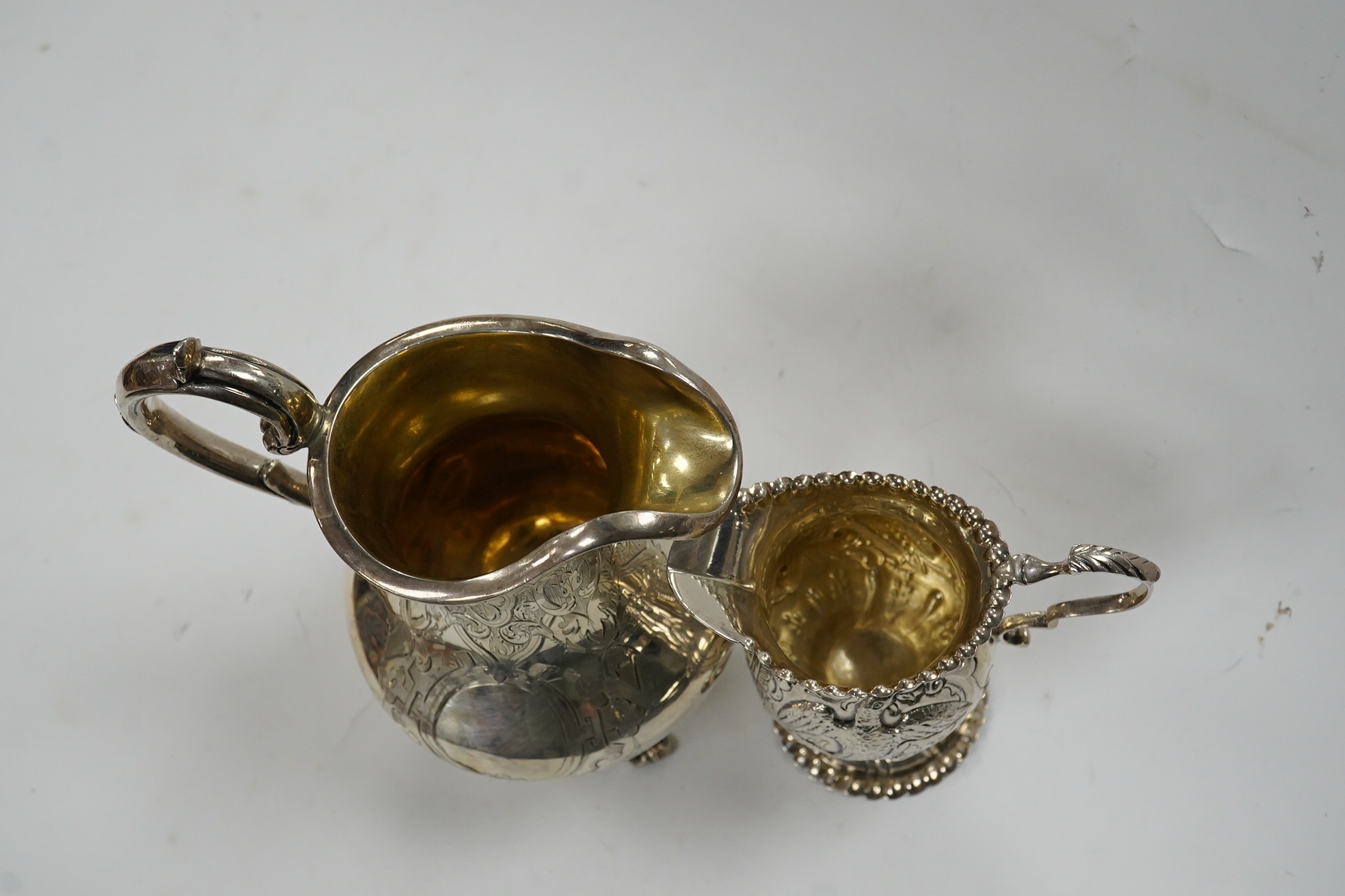 A Victorian engraved silver baluster cream jug, Henry Holland, London, 1862, 15cm, together with an Edwardian embossed silver cream jug, London, 1902, 10.5oz. Condition - poor